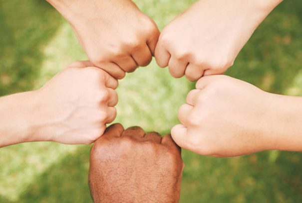 Multiethnic hands fist bumping outside in nature. Closeup of a group of people celebrating by fist bumping. Closed hands in a circle